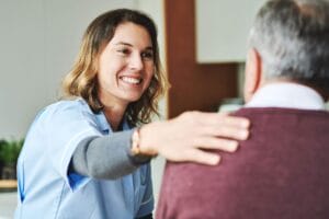 A woman caregiver puts her hand on the shoulder of an older adult man.