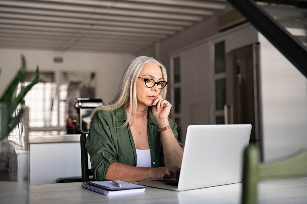 An older adult woman is using her laptop, looking concerned.