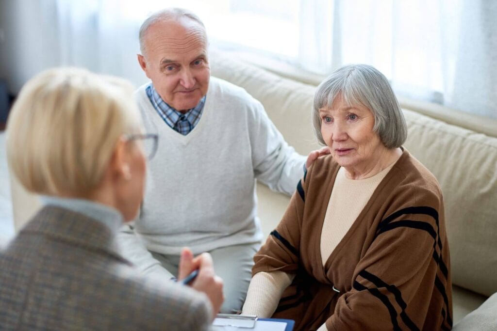 An older adult man and woman consult with a woman holding a clipboard.