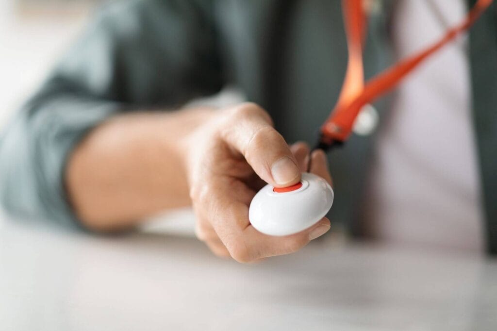 A hand is shown pressing a wearable medical alert button.