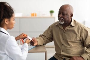 A woman doctor hands a medical alert system button to an older adult man seated across from her.