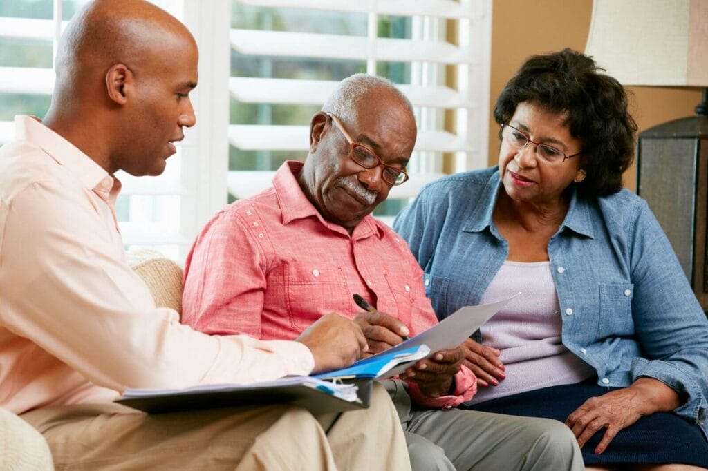 An older adult man and woman sit on a couch looking over paperwork with a younger man.