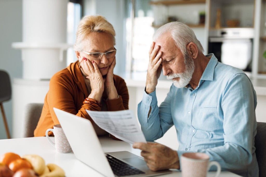 Concerned mature couple look at information on paper and their laptop computer screen.