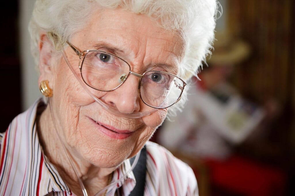 A woman breathing oxygen through a nasal cannula smiles at the camera.