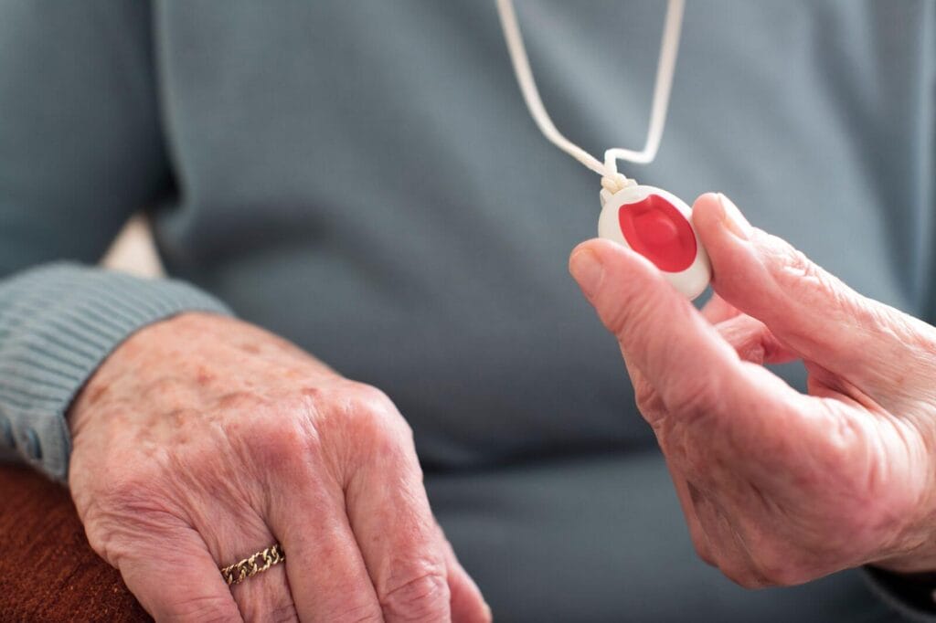 A close-up of an older adult woman's hand holding a wearable medical alert system emergency button.