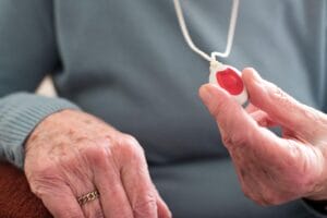 A close-up of an older adult woman's hand holding a wearable medical alert system emergency button.