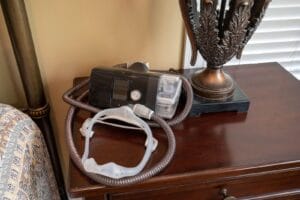 A CPAP machine, tubing, and mask sit on a bedside table.