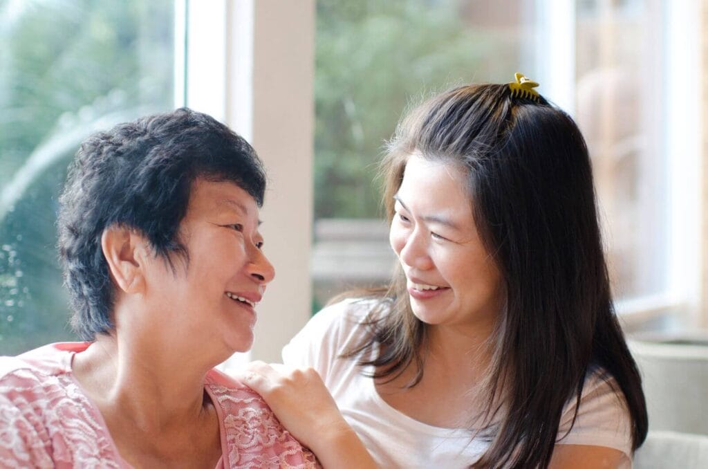 An older adult woman and her daughter look at each other, smiling.