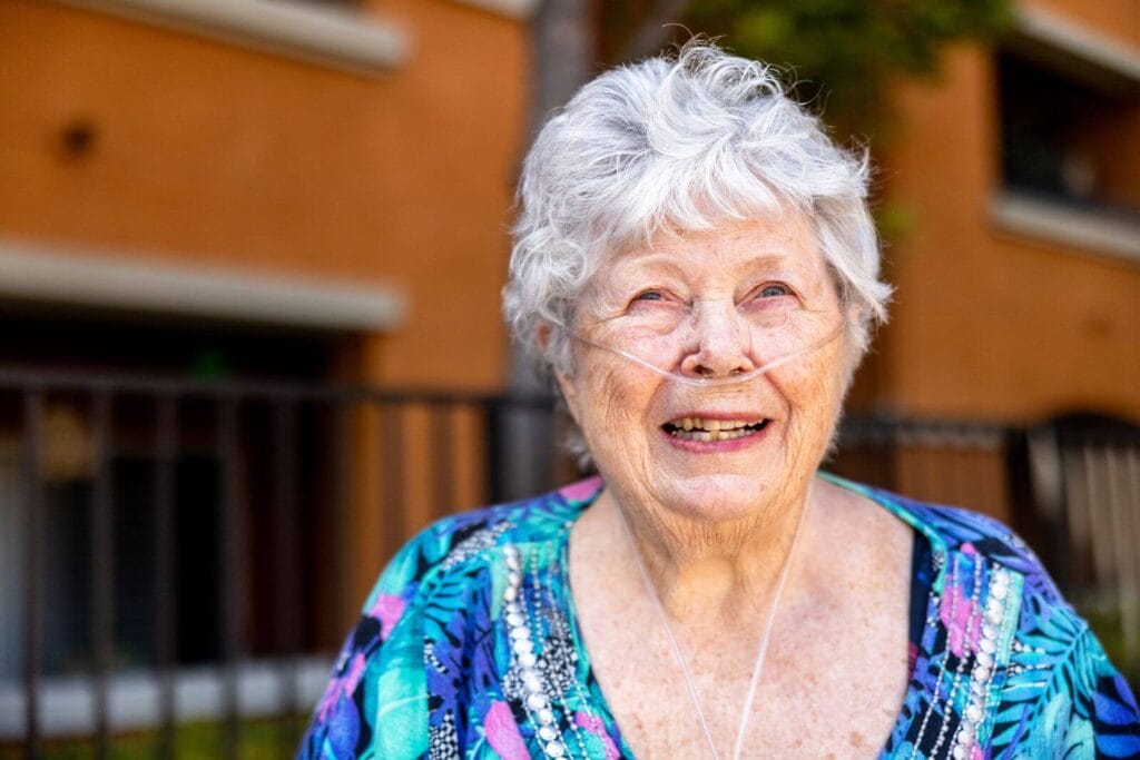 An older adult woman breathing oxygen through a nasal cannula smiles.