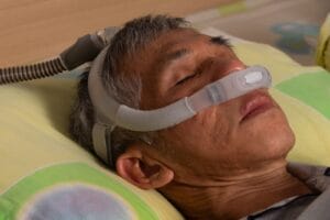 Close-up of a sleeping man's face. He is wearing a CPAP machine mask on his nose.