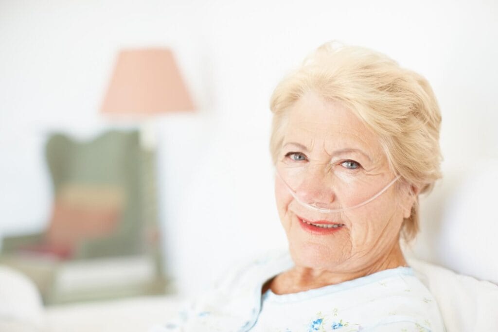 An older adult woman with a nasal cannula smiles at the camera.