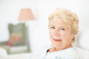 An older adult woman with a nasal cannula smiles at the camera.