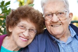An older adult man and woman smile at the camera. The man is wearing a nasal cannula for supplemental oxygen.