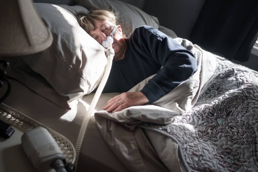 An older adult woman is sleeping in bed with a CPAP mask on her face.