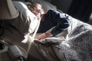 An older adult woman is sleeping in bed with a CPAP mask on her face.