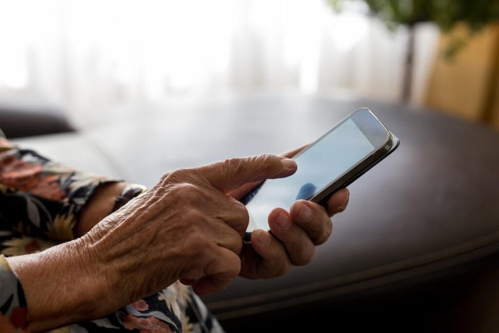 The hands of an older adult are shown holding a smartphone.