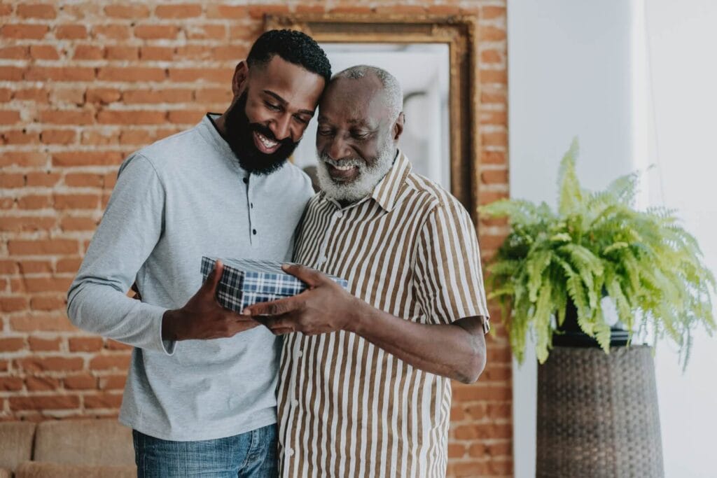 A man gives his older adult father a gift in a box.
