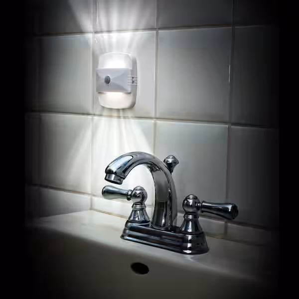 A bathroom sink faucet is illuminated by a nightlight. The nightlight is slim and from it emanates light above and below to give the user light to safety move through the bathroom at night.