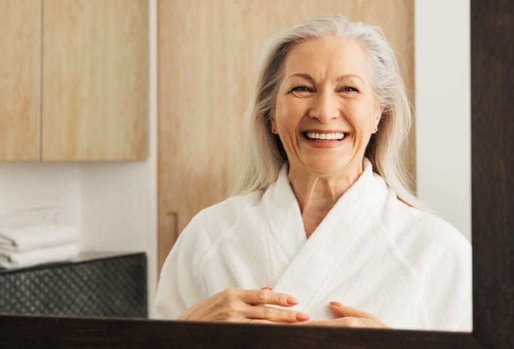 An older adult woman wearing a bathrobe smiles at the camera.