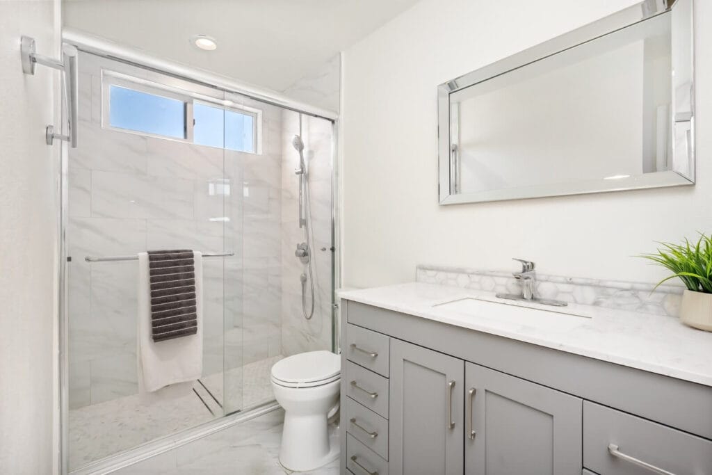 Image of a bathroom. The bathroom features a vanity with a sink, a mirror, a toilet, and a walk-in shower.