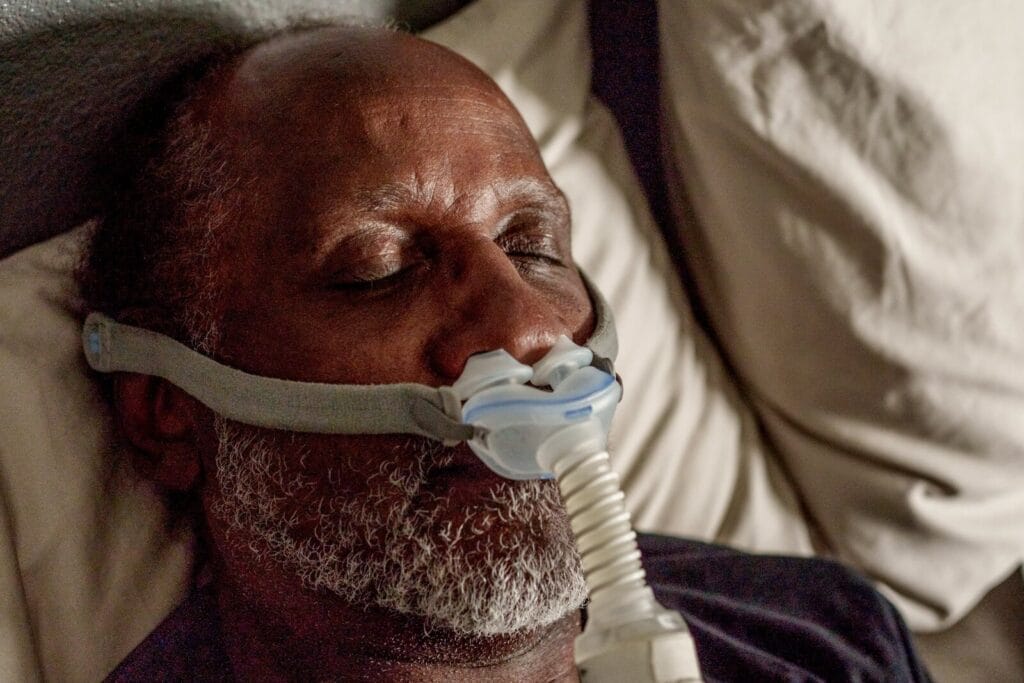 An older adult man sleeps with a CPAP mask on his face.