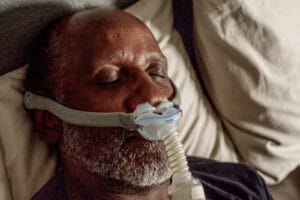 An older adult man sleeps with a CPAP mask on his face.