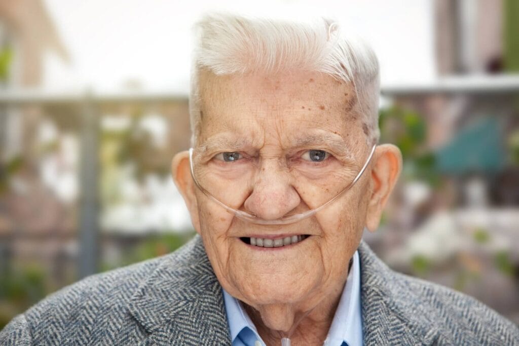 An older adult man wearing a nasal cannula for oxygen smiles at the camera.