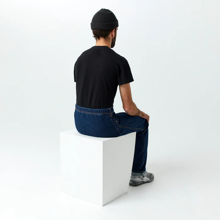 Image from behind a man who is seated on a block. He is wearing IZ Adaptive seamless jeans, which have an elastic waistband and no seams or pockets on the backside.