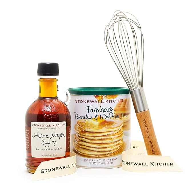 Photo of Stonewall Kitchen brand Maine maple syrup in a bottle, pancake and waffle mix in a canister, and a whisk.
