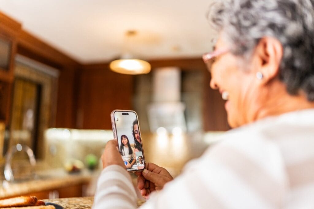 An older adult woman is using the video chat feature on her smartphone to talk with her daughter and granddaughter.