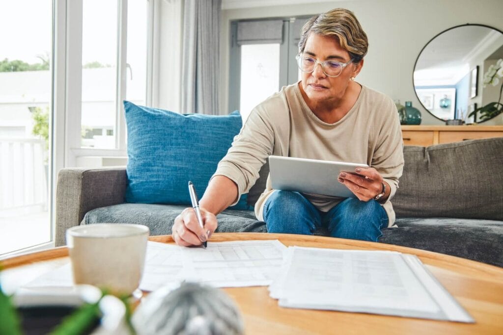 A woman sits on her couch, working on paperwork on the coffee table in front of her.