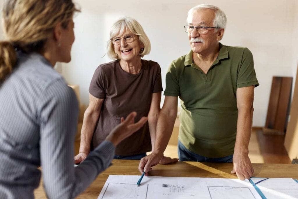 An older adult man and woman speak with a woman who is showing them floorplans for home modifications.