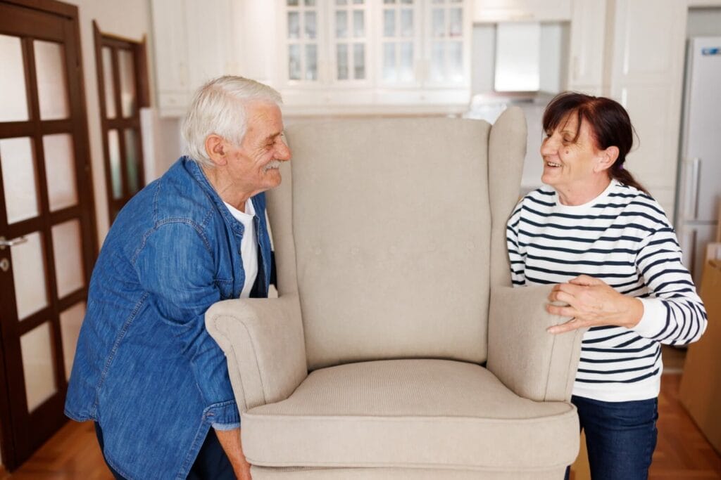 An older adult man and woman carry an armchair.